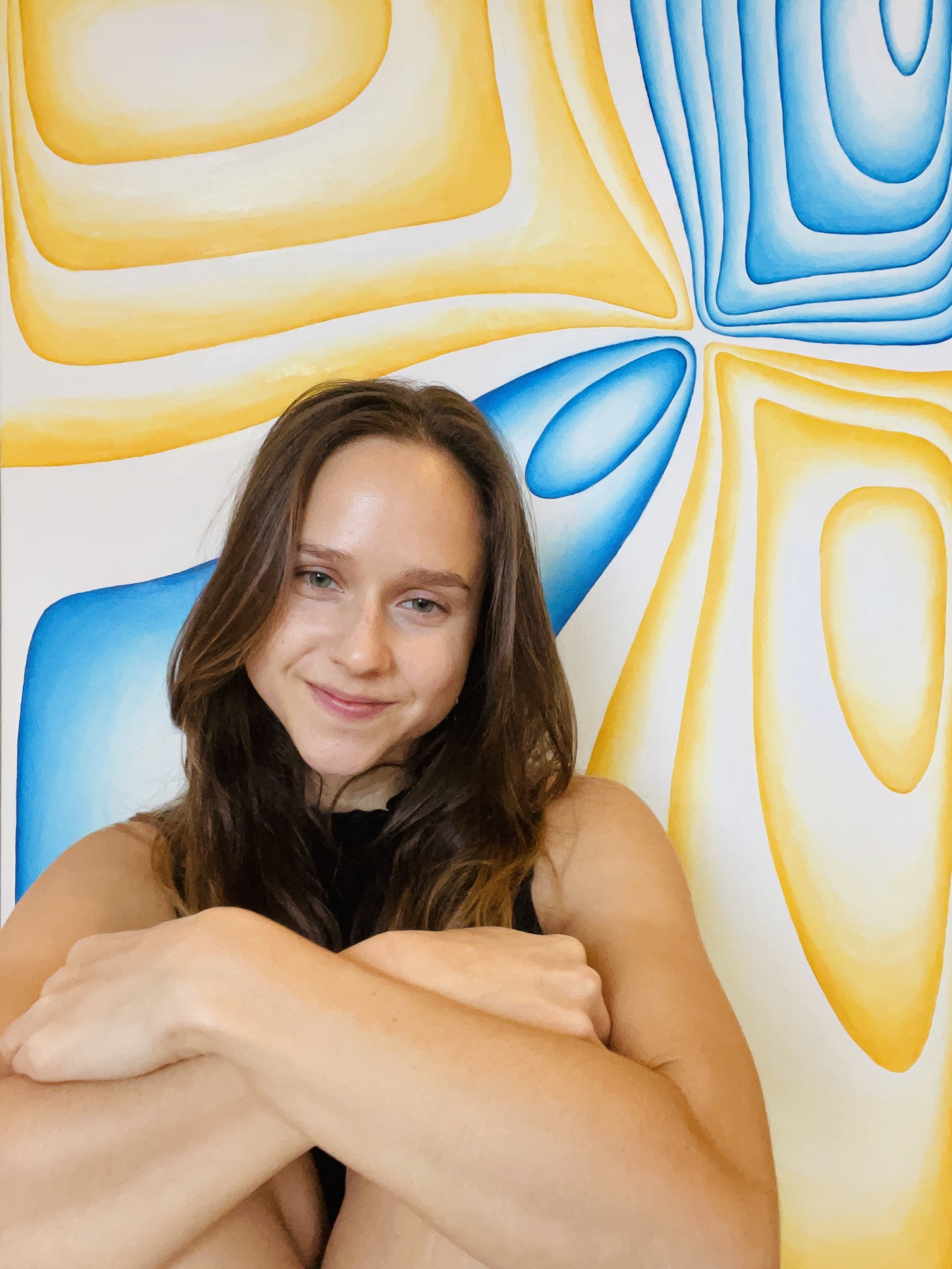 Portrait of artist Kristina Flegler in front of her abstract oil painting 'Static Harmony', featuring blue and yellow contour forms